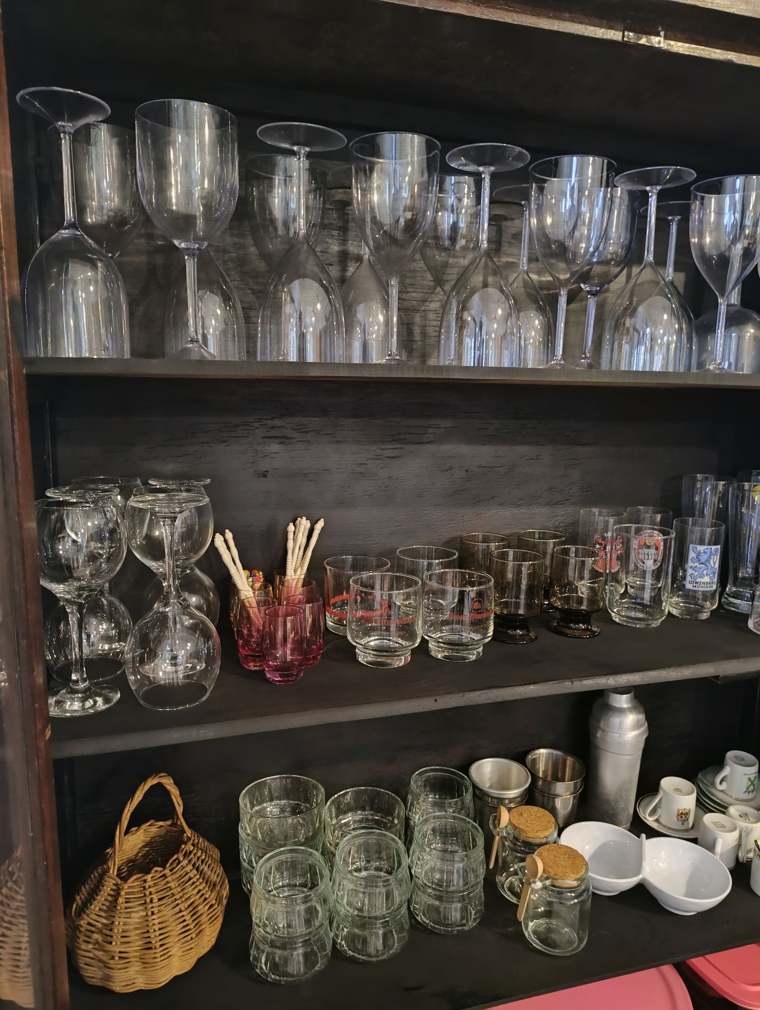 A shelf with various glassware, including wine glasses, tumblers, and shot glasses.