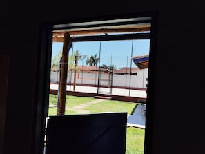 A view through a window with a metal gate, a grassy yard, and a building with a red roof in the background.