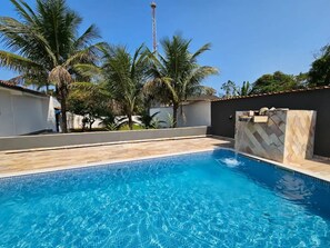 Piscina con agua azul cristalina, rodeada de palmeras y un muro de piedra.