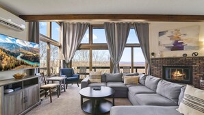 A cozy living room with a large TV, a fireplace, and a scenic view through the windows. - Pocono Mountains Camelback Retreat-Stunning Views (Tannersville)