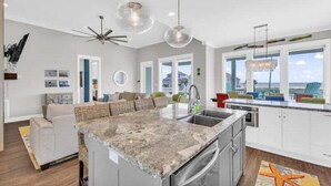 A modern kitchen with a central island, white cabinetry, and a view of the ocean. - Beach View 4BR | Sleeps 14 | Fenced Yard (Crystal Beach)