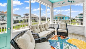 A covered outdoor area with a sofa and chairs, large windows, and a view of other buildings. - Beach View 4BR | Sleeps 14 | Fenced Yard (Crystal Beach)
