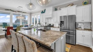 A spacious kitchen with white cabinets, a large island, stainless steel appliances, and pendant lighting. - Beach View 4BR | Sleeps 14 | Fenced Yard (Crystal Beach)