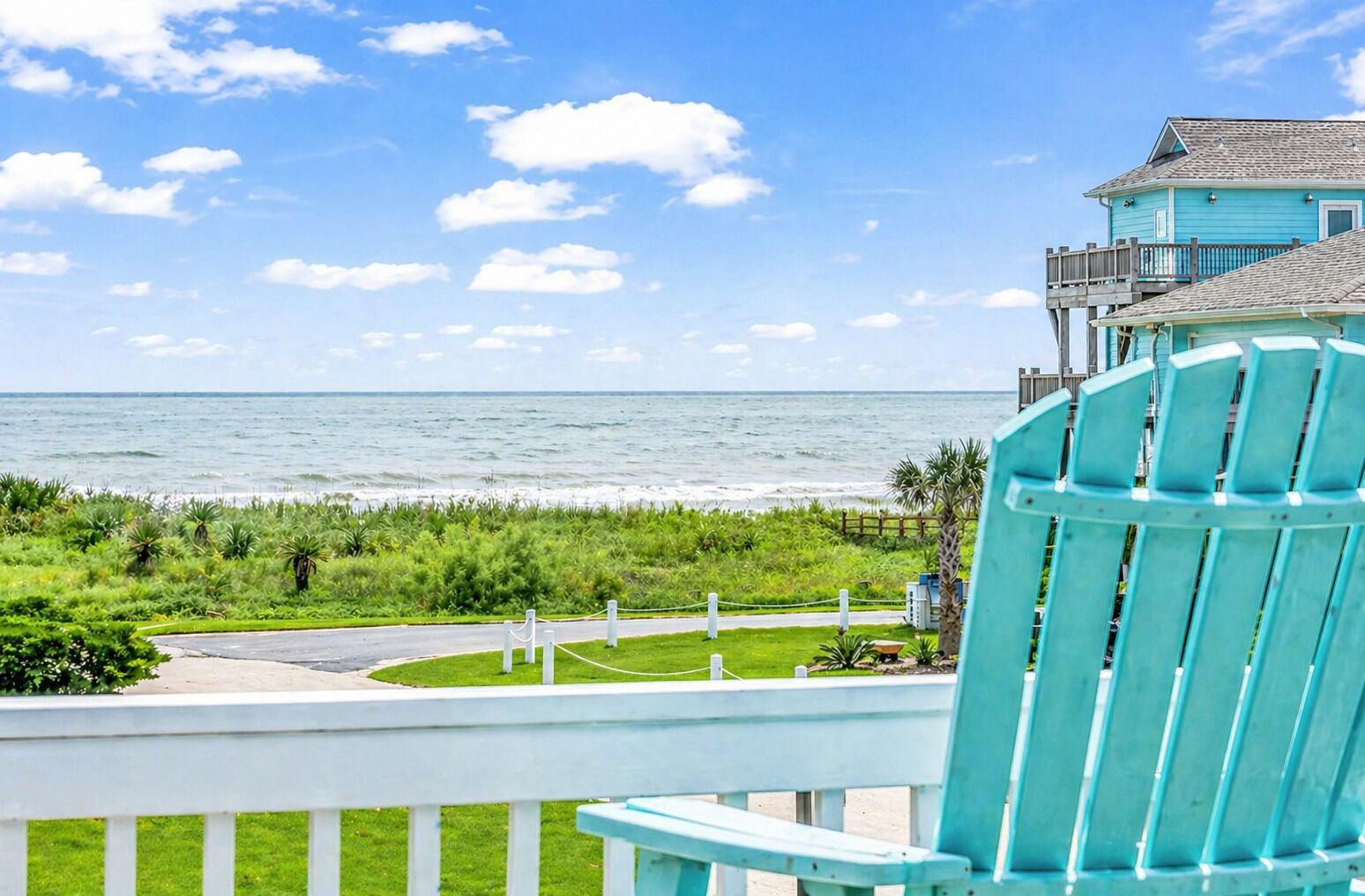 Une chaise turquoise donnant sur une plage, avec vue sur l’océan et un bâtiment doté d’un balcon.