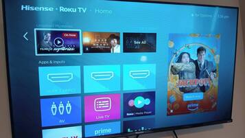A Hisense TV displaying the Roku TV Home screen with various streaming apps and content options.