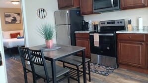 A compact kitchen with wooden cabinets, a stainless steel refrigerator, a microwave, and a stove. There is a dining table with chairs and a potted plant on the counter. - The Micro-Loft at Mt. Pleasant New 2BR APT Parking (Providence)