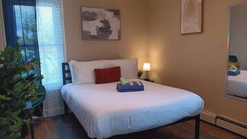 A hotel room with a bed, a nightstand, a lamp, a plant, and artwork on the walls.