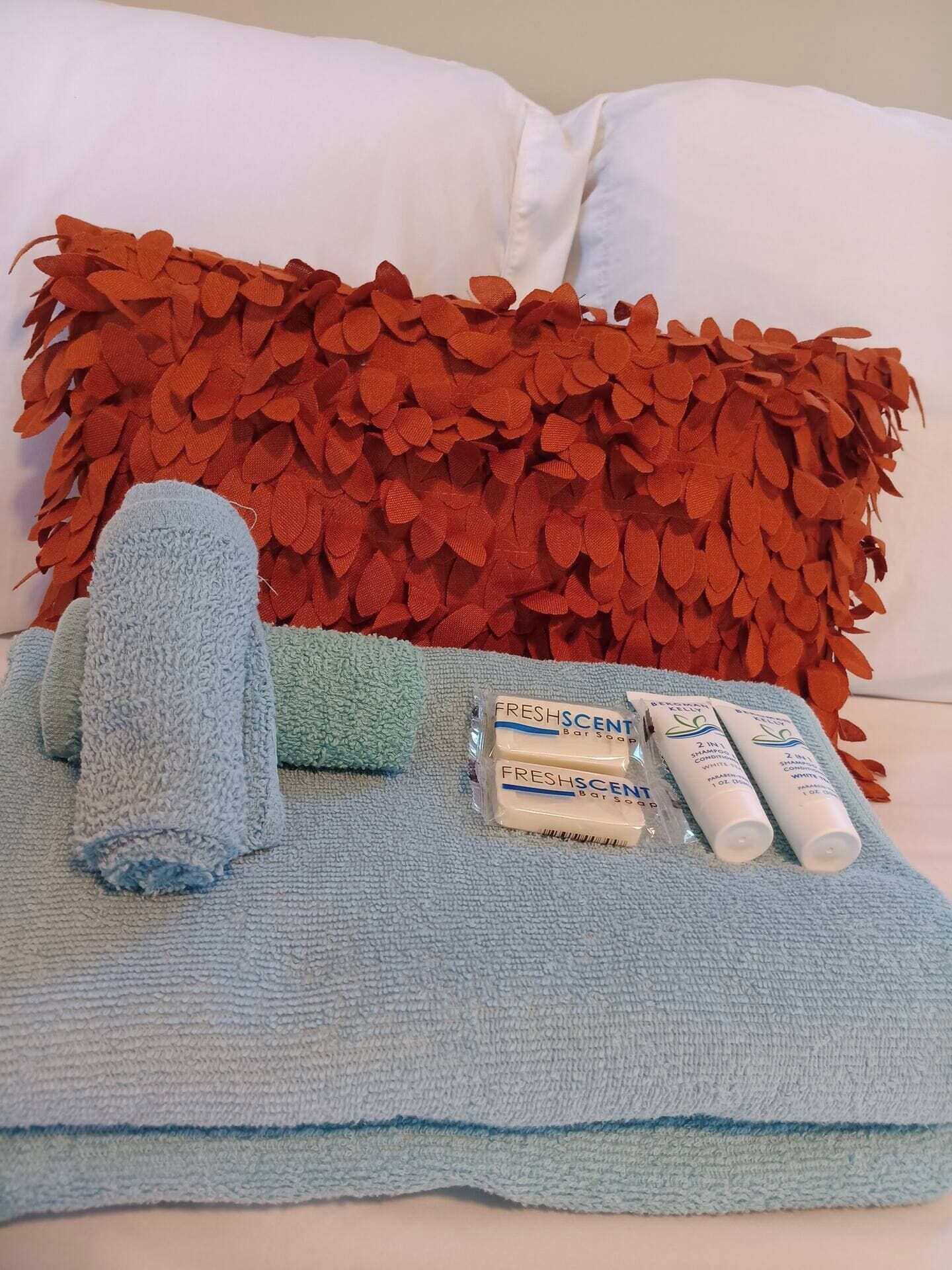 A neatly arranged bathroom with a blue towel, a green towel, and two bottles of FreshScents bar soap on a white surface.