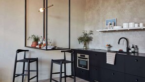 A modern kitchen with a black countertop, two bar stools, a hanging light fixture, and a built-in oven. - Extrados Loft King Suite (Philadelphia)