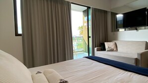 A hotel room with a bed, a sofa, a TV, and a balcony view. - Mana Beach Experience 217Aloha byLaPlaya (Ipojuca)