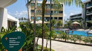 A hotel with a swimming pool, palm trees, and a sign indicating amenities like a restaurant and a sports center. - Mana Beach Experience 217Aloha byLaPlaya (Ipojuca)