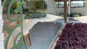 An outdoor area with a glass wall, a wooden bench, and a landscaped garden with purple foliage. - Mana Beach Experience 217Aloha byLaPlaya (Ipojuca)