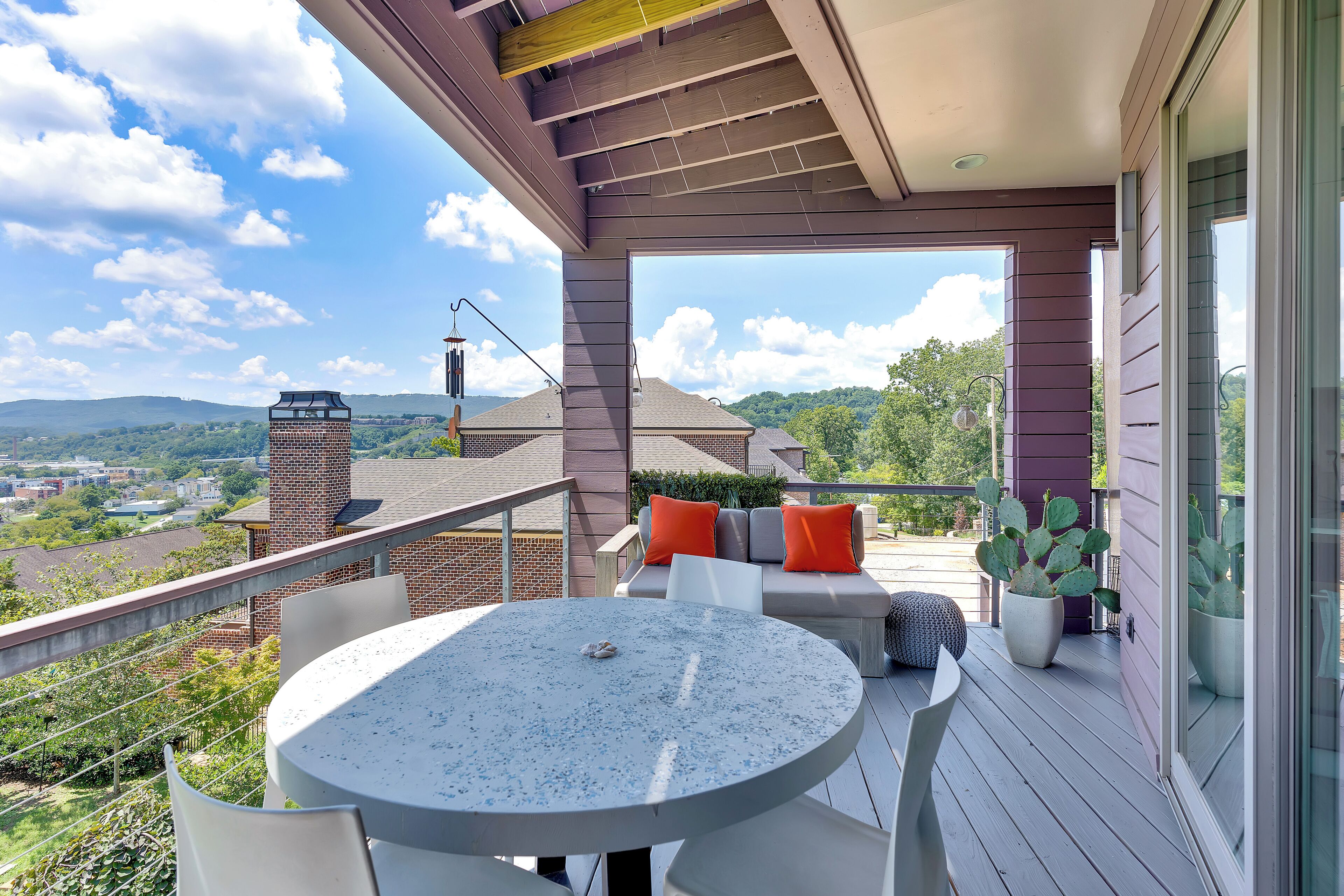 Un balcon avec une table ronde et des chaises, un coin salon confortable avec des coussins, et une vue sur le paysage environnant.