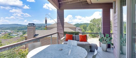 Un balcon avec une table ronde et des chaises, un coin salon confortable avec des coussins, et une vue sur le paysage environnant.