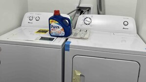 Lavadora y secadora de carga frontal blancas, con una botella de detergente Purex azul encima.