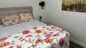 Un dormitorio con cama, ropa de cama floral, una mesita de noche, una lámpara de pared y un cuadro.