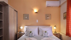 A neatly made bed with white linens and decorative pillows, a bedside lamp, and a wall-mounted air conditioner.