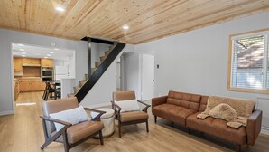 Un salon moderne avec un plafond en bois, un escalier, un canapé en cuir marron et un coin repas doté de meubles de rangement en bois.