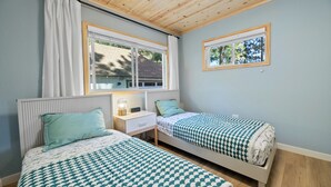 Une chambre avec deux lits simples, une table de chevet, une lampe et une fenêtre avec des rideaux.