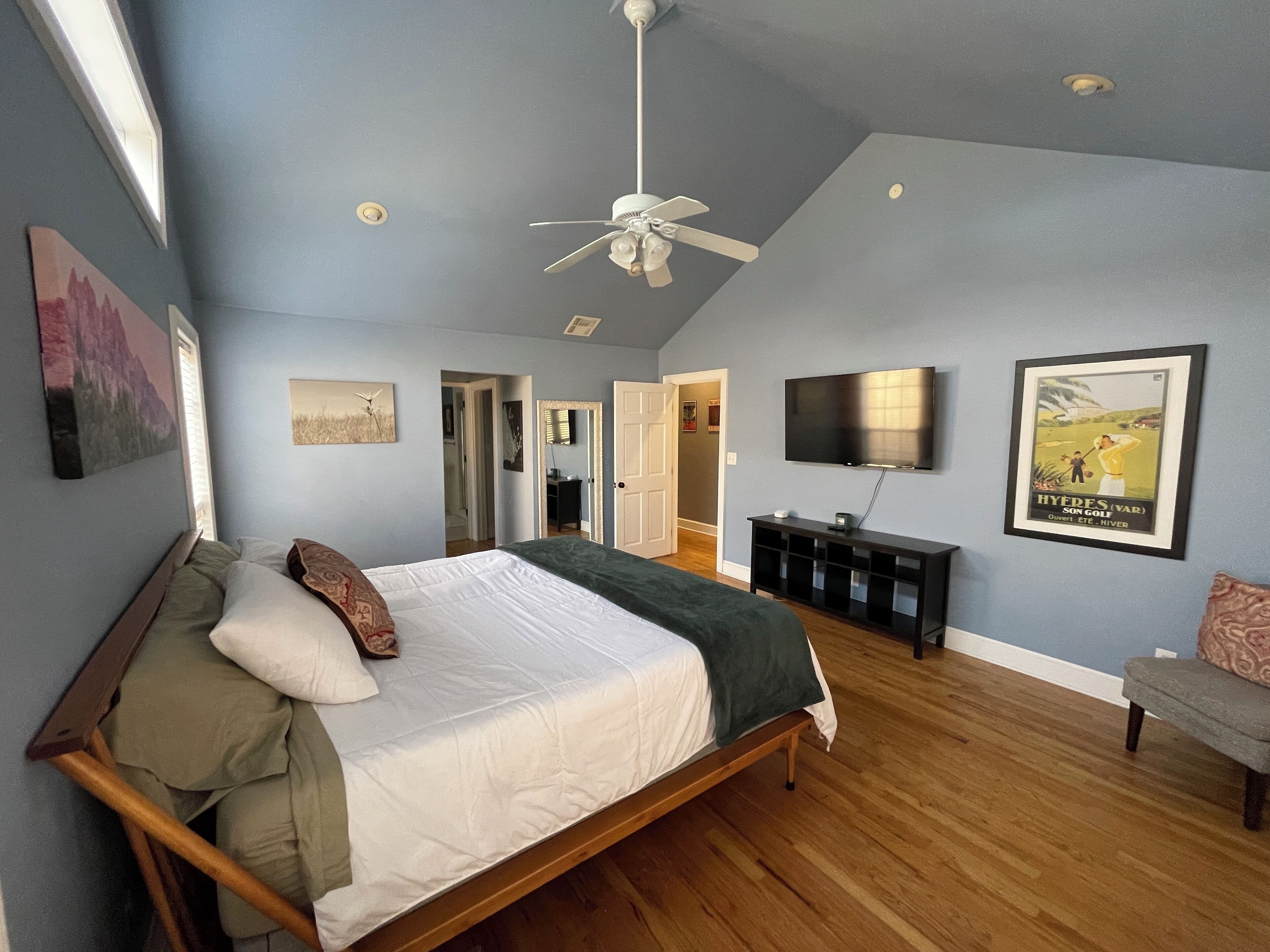 A bedroom with a bed, a ceiling fan, a TV, and a framed picture on the wall.