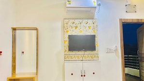 A room with a mounted flat-screen TV on a floral-patterned wall, a wooden cabinet below, and an air conditioning unit above. - Hotel Shri Salasar (Ujjain)