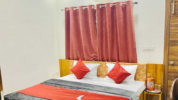 A hotel room with a wooden bed, red curtains, a ceiling fan, an air conditioning unit, and a wooden wardrobe. - Hotel Shri Salasar (Ujjain)