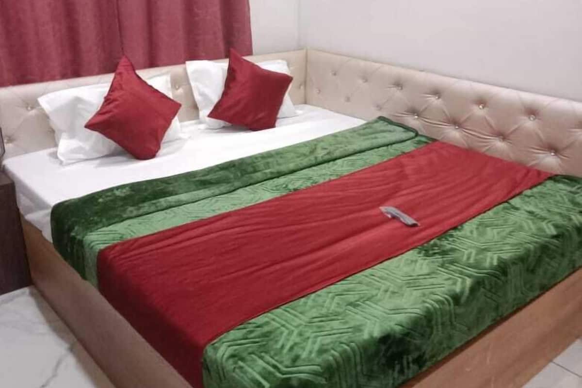 Ein Bett mit einem beige gefärbten Kopfteil, weißer Bettwäsche und dekorativen Kissen in Rot und Grün.