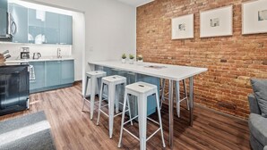 A modern kitchen with a brick wall, a white island with bar stools, and a grey sofa. - Cozy&Modern 2Bdr Apt PIttsburgh (Pittsburgh)