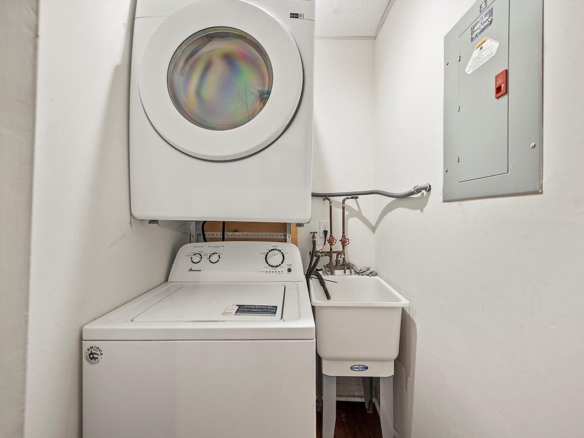 A compact laundry room with a front-loading washer and dryer, a small sink, and a utility meter on the wall.