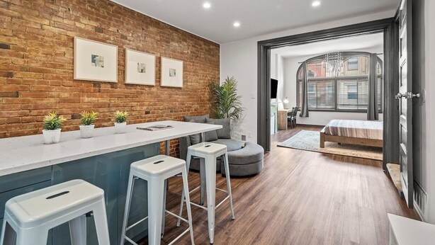A modern kitchen with a brick wall, white bar stools, and a dining area with a grey sofa. - Cozy&Modern 2Bdr Apt PIttsburgh (Pittsburgh)