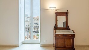 A room with a wooden vanity, a mirror, and a view of buildings through a glass door. - Palazzo Pupillo Liberty Suite (Syracuse)