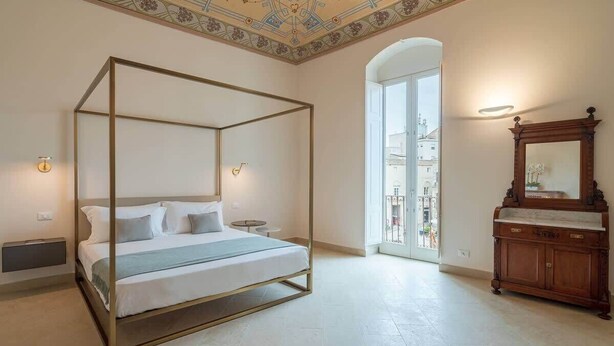 A four-poster bed with a view of the city through a large window. - Palazzo Pupillo Liberty Suite (Syracuse)