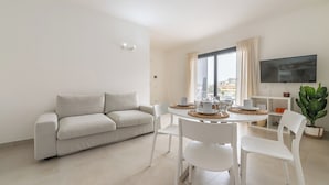 Uma sala de estar moderna com sofá, mesa de jantar, cadeiras, televisão e janela com cortinas.