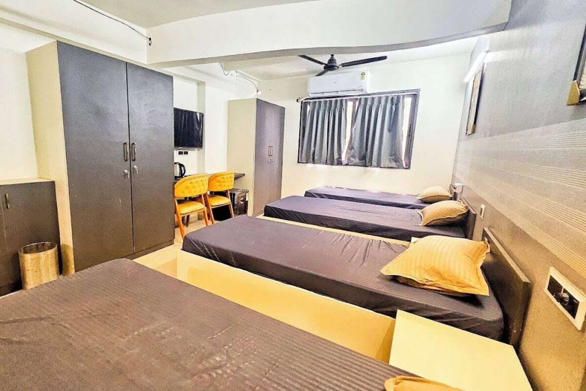 Ein kleines Hotelzimmer mit drei Einzelbetten, einem kleinen Schreibtisch mit Stuhl, einem Kleiderschrank und einem Deckenventilator.