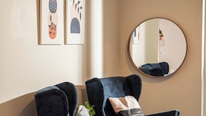 A modern living room with two dark blue armchairs, a round mirror, and artwork on the wall. - Charming studio with reading nook & city view (Nicosia)