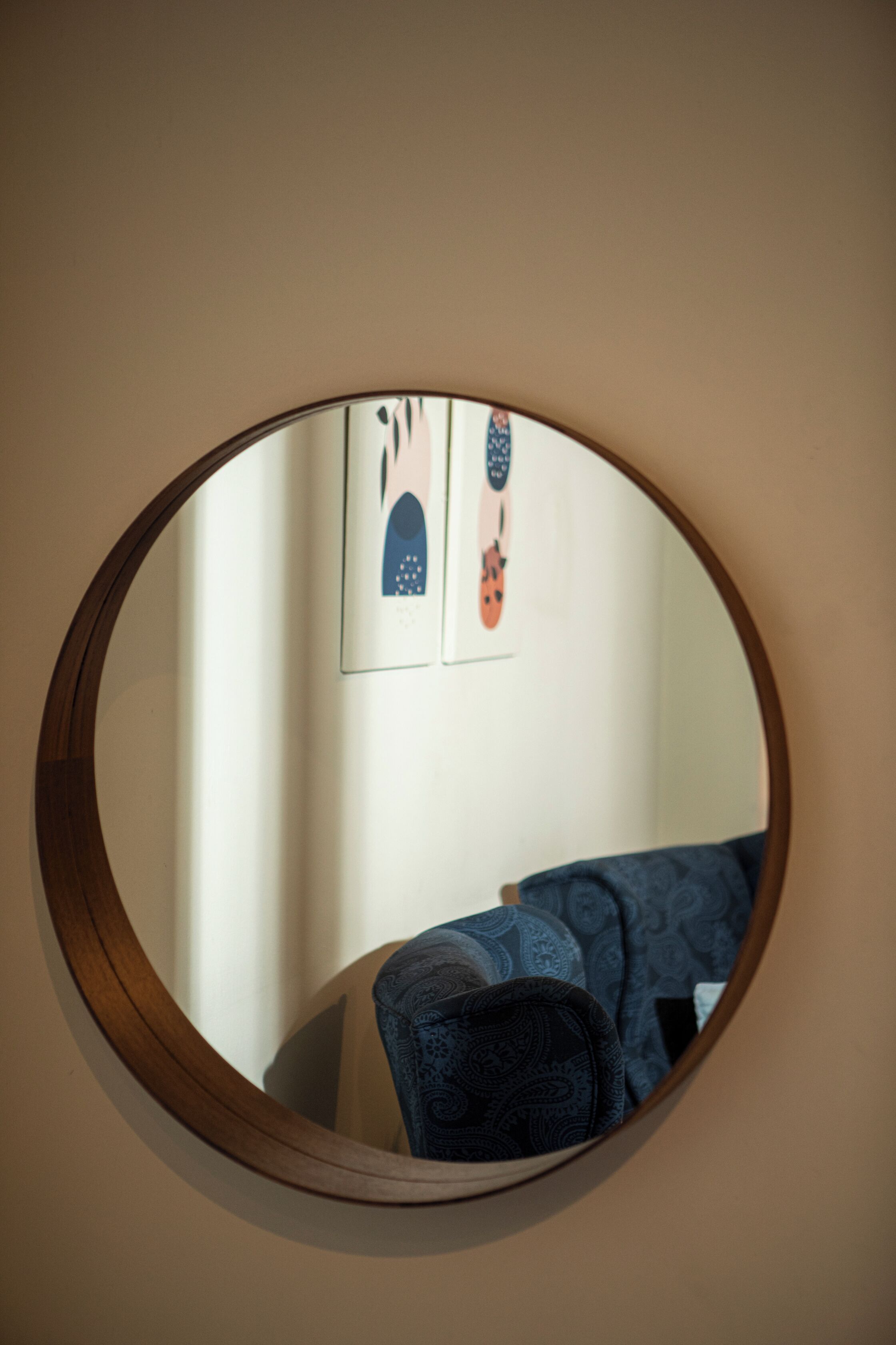 Un miroir rond est accroché au mur, et en arrière-plan, on aperçoit un canapé à motifs et deux tableaux encadrés.