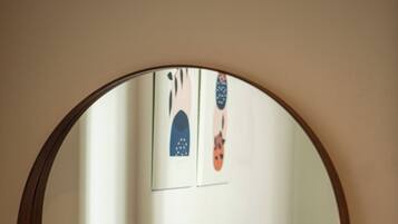 Un miroir rond est accroché au mur, et en arrière-plan, on aperçoit un canapé à motifs et deux tableaux encadrés.