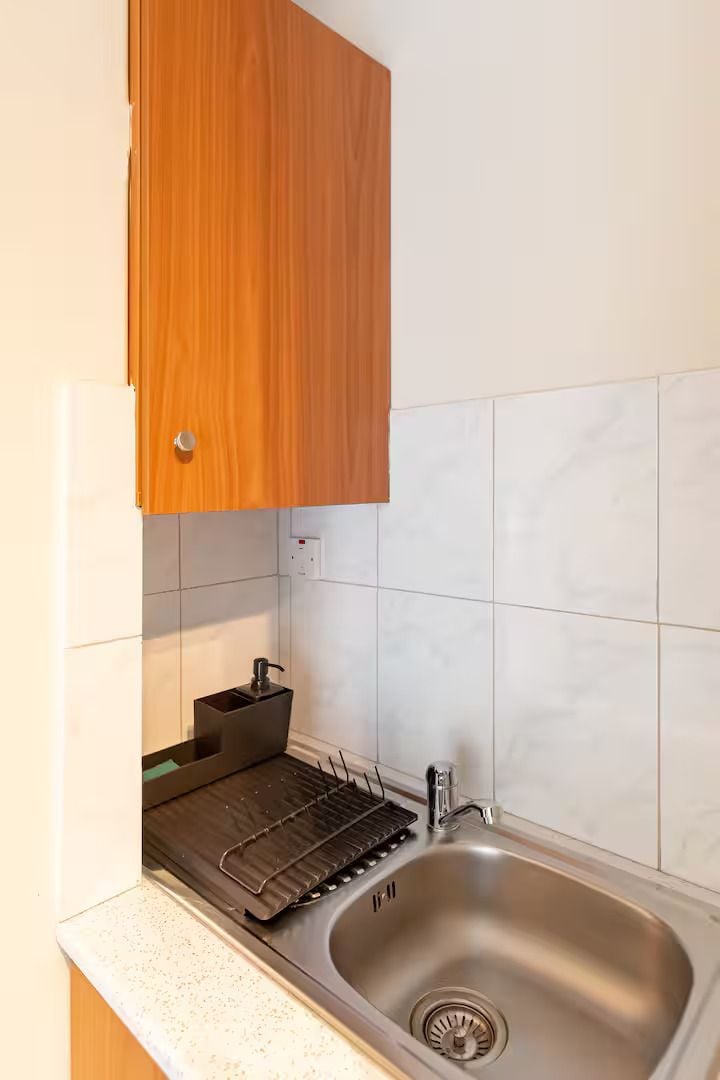 A kitchen with a stainless steel sink, a drying rack, and wooden cabinets.