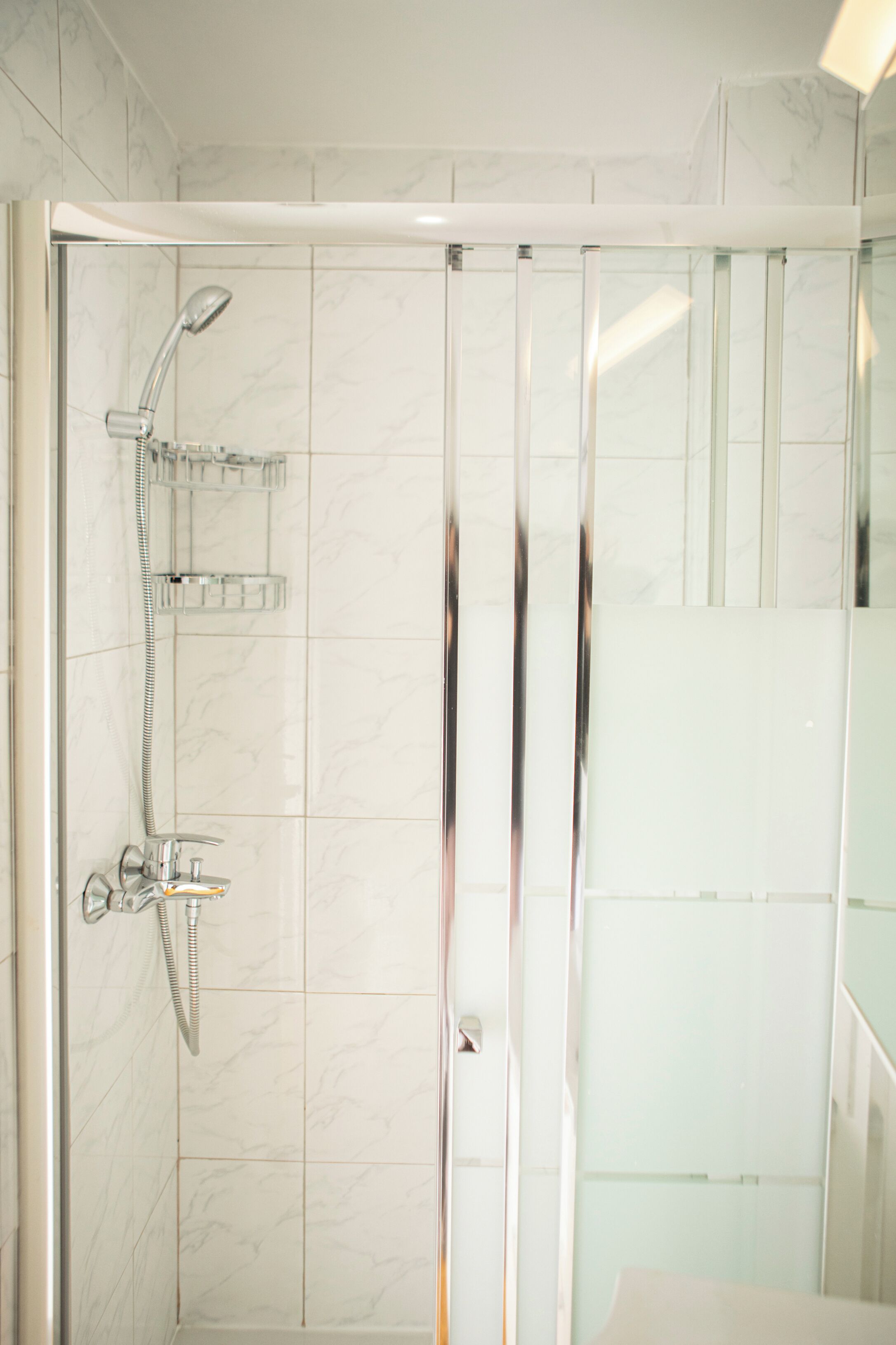A modern bathroom with a glass shower enclosure, a handheld showerhead, and a built-in shelf.