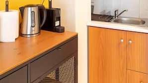 A kitchen with a yellow wall, wooden cabinets, a sink, and a kettle on the counter. - Charming studio with reading nook & city view (Nicosia)