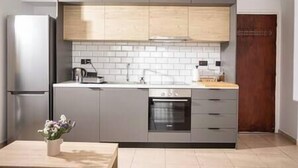 Una cocina moderna con gabinetes grises, salpicadero de azulejos blancos, refrigerador de acero inoxidable, horno empotrado y encimera de madera.