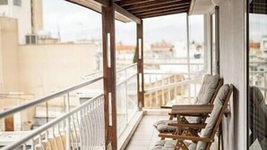 Un balcón con dos sillones de madera y una mesita, con vista a la ciudad.