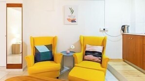 Een kamer met twee gele fauteuils, een klein tafeltje met een lamp en een houten kast.