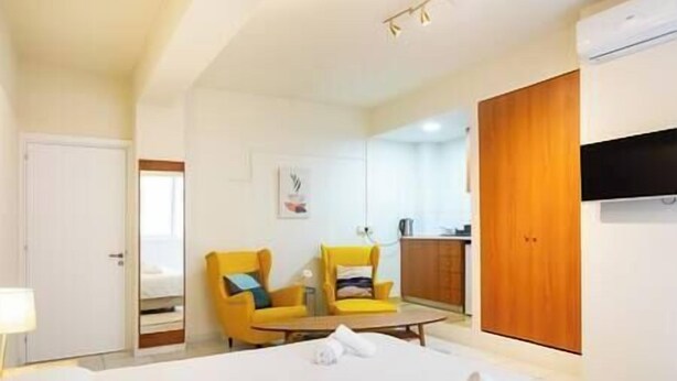 Een hotelkamer met een bed, twee gele fauteuils, een houten garderobe en een televisie.