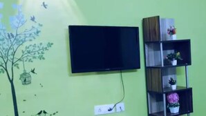 Un téléviseur fixé au mur, une prise de courant et une étagère avec des objets décoratifs.