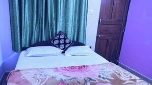 Un lit avec une couvre-lit à motifs floraux, deux oreillers et un rideau vert foncé.