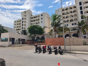 Hotel com vários andares, varandas, motocicletas estacionadas e palmeiras.