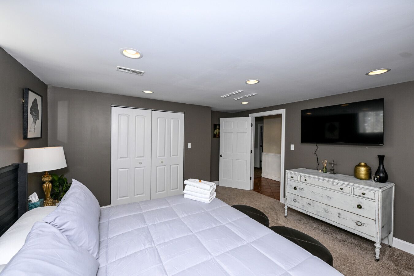 A bedroom with a bed, a dresser, a TV, and a door leading to another room.