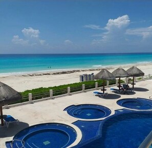 A pool area with multiple circular pools, a beach view, and thatched umbrellas. - ESTUDIO 25 VILLAS MARLIN IDEAL PARA PAREJAS  ACCESO A PLAYA Y PISCINAS  (Cancún)