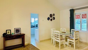 A dining area with a glass table, white chairs, a wooden bench, and a patterned ceiling light. - Hoopoe House (Ootacamund)